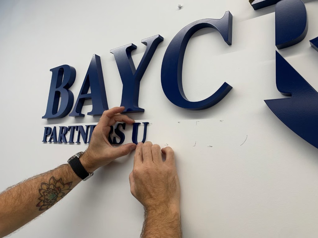 Installer mounting BAYC Partners navy 3D lettering on a white wall