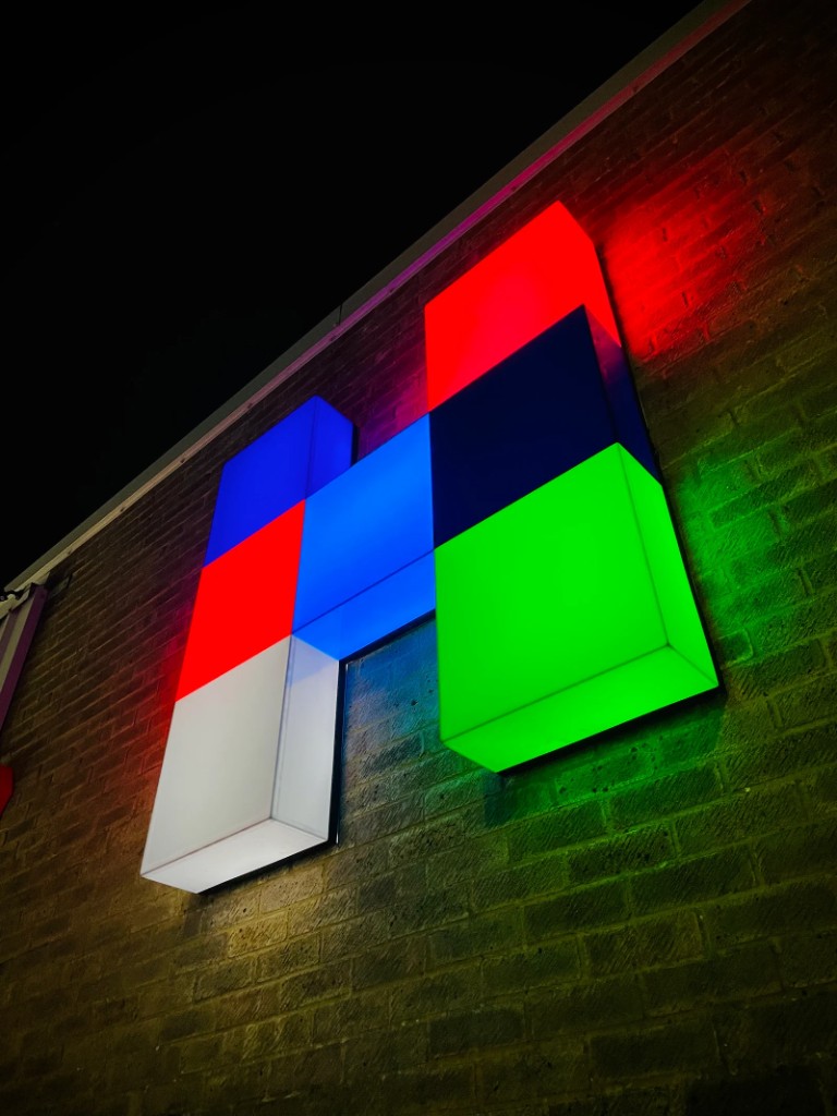 Face-illuminated multicolour 3D lettering on a brick wall at night