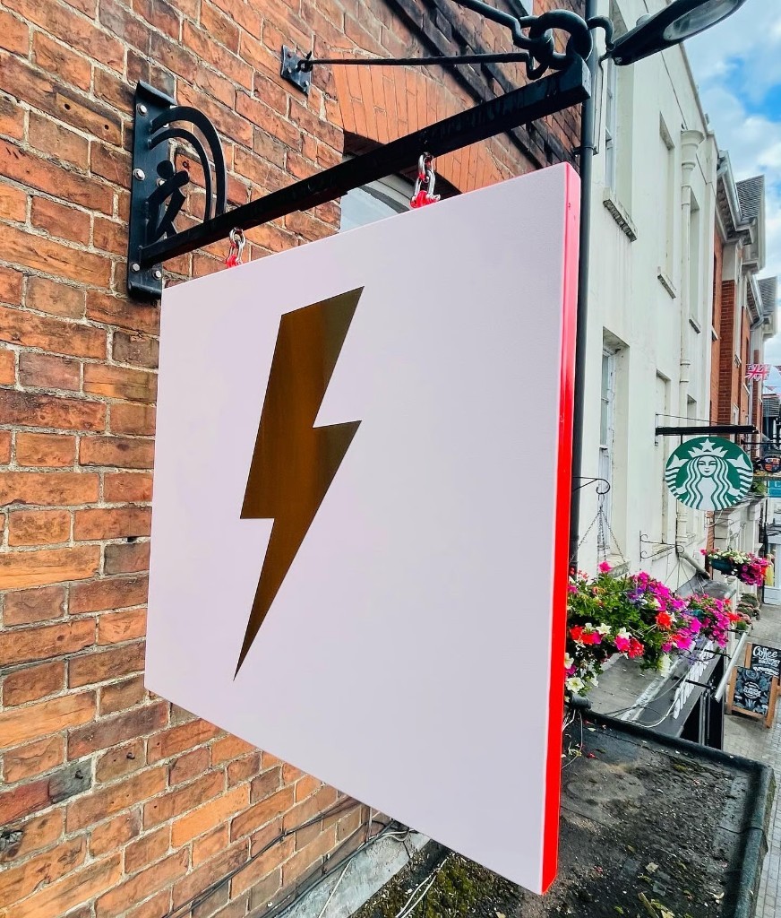 Square blade projecting sign with gold lightning bolt on a brick frontage