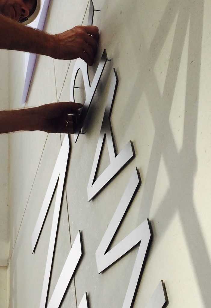 Close-up of brushed metal Marist lettering being mounted on stand-offs
