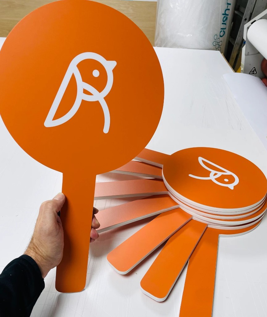 Bright orange branded paddle signs with white logo, ready for handover