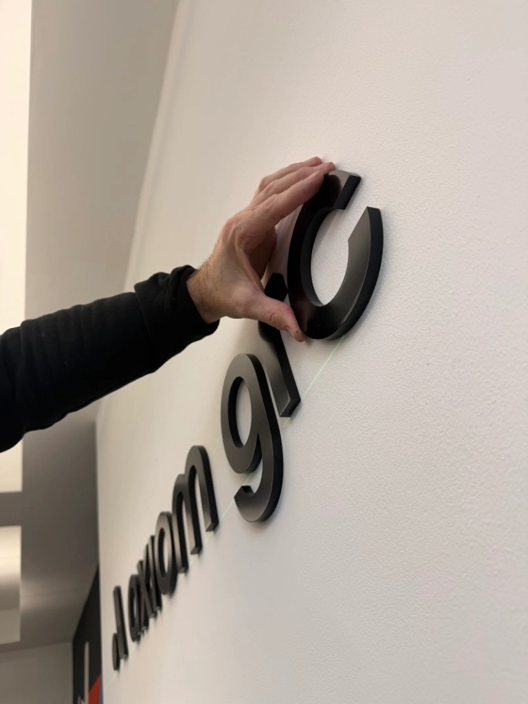 Installer aligning black 3D lettering with a green laser level on an office wall