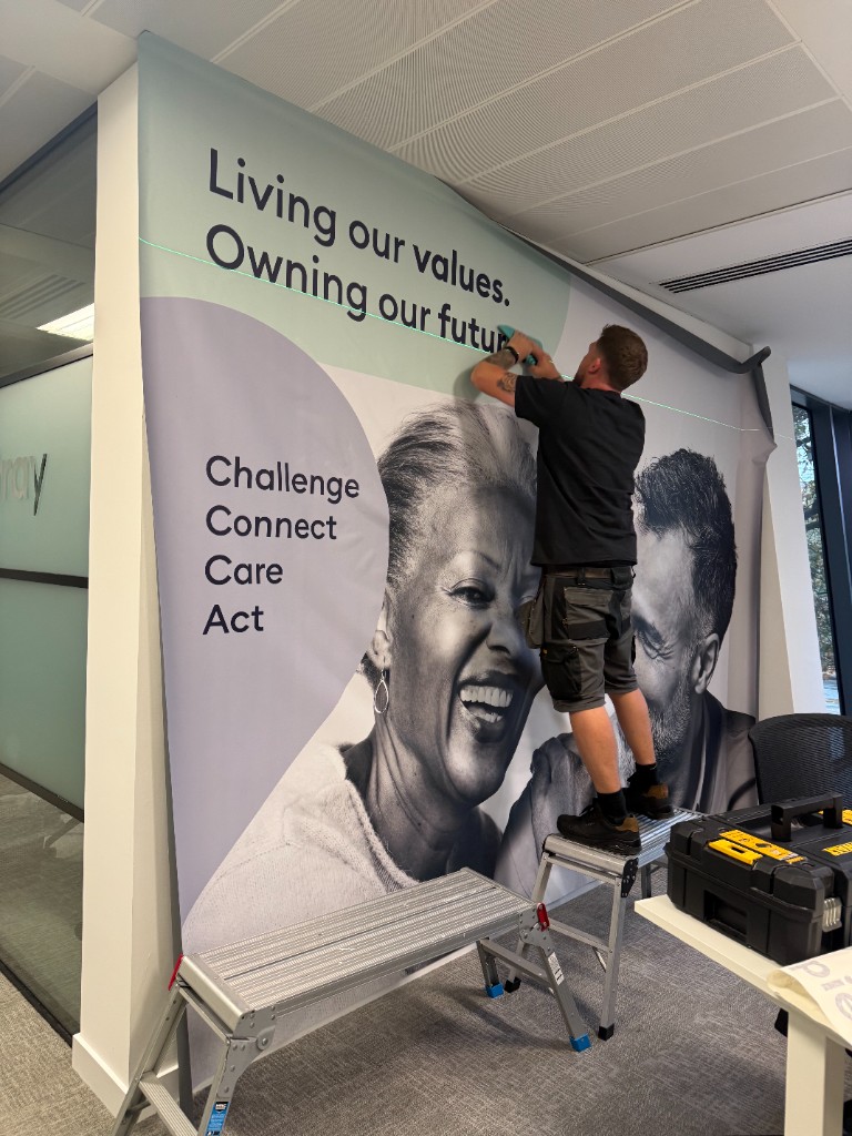 Installer fitting a large printed wall mural in a live office